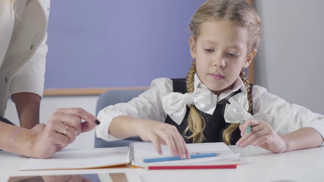 迷人的白人女学生的肖像用红铅笔写，而不认识的老师站在她旁边。孩子在家学习，有家教。研究、教育、勤奋。视频素材