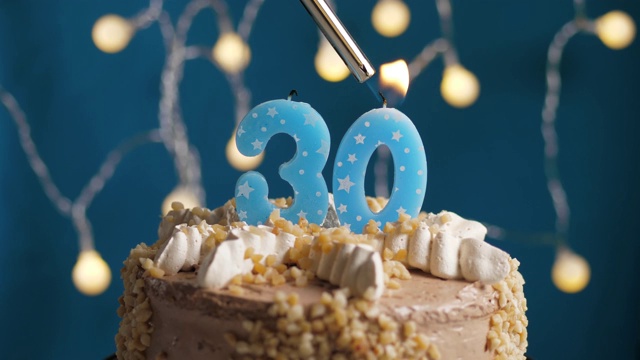 生日蛋糕与30号蜡烛在蓝色的背景。蜡烛被点燃了。慢动作和近景视频下载