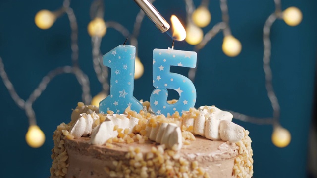 蓝色背景上15号蜡烛的生日蛋糕。蜡烛被点燃了。慢动作和近景视频下载