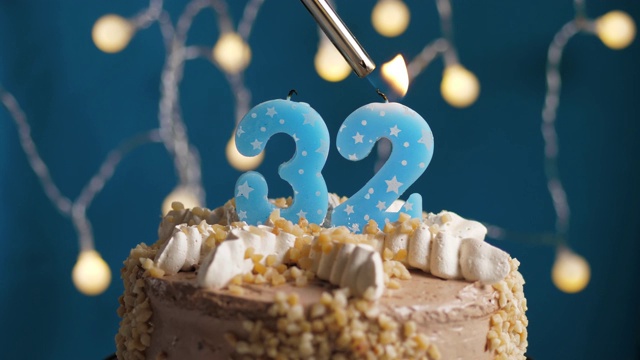 蓝底32号蜡烛生日蛋糕。蜡烛被点燃了。慢动作和近景视频素材