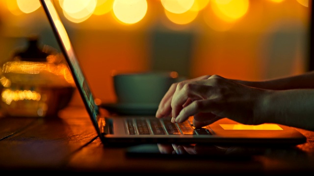 女性的手指在半暗的温暖设置下在笔记本电脑上打字。明亮的黄色圆形散景背景。滑动,4 k视频素材