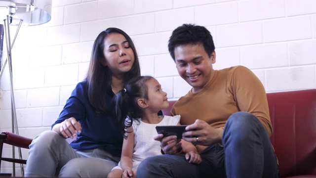 幸福年轻的亚洲家庭坐在客厅的沙发上用智能手机自拍，家庭放松和一起在家里度过时间视频素材