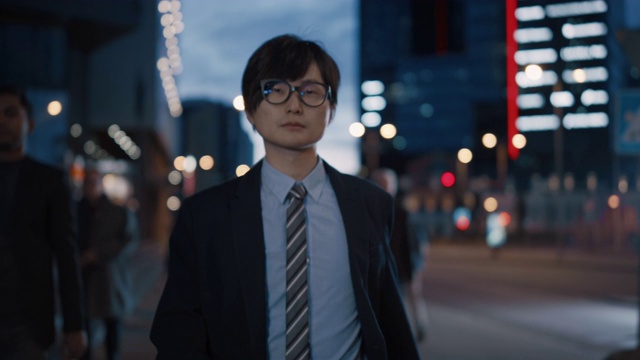 穿着西装的年轻日本商人走在街上。其他在办公室上班或回家的人。它是清晨或傍晚。城市灯光与摩天大楼的背景视频素材