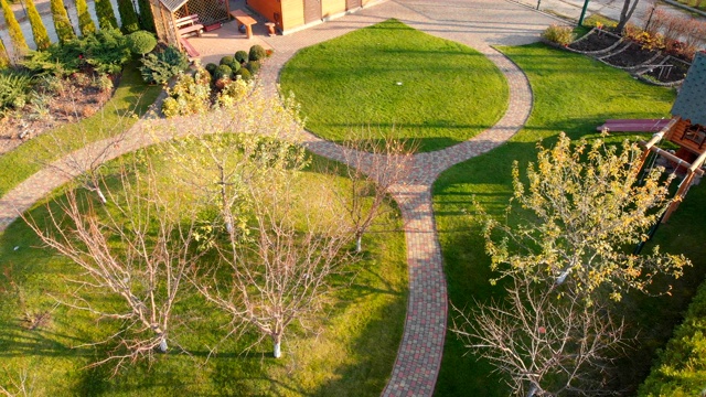 无人机鸟瞰后院的果园，圆形的石头小路，绿色的草坪小山和树木。景观设计和园艺。视频下载