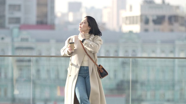 自信的白人妇女的肖像在优雅的米色外套在城市休息。年轻成功的女商人站在摩天大楼的背景下看向别处。电影4k ProRes总部。视频素材