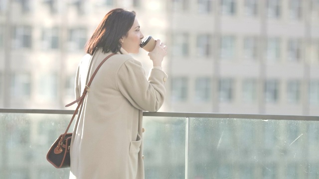 侧面背面的年轻白人妇女在优雅的大衣喝咖啡在城市的户外。成功自信的女商人正在休息。电影4k ProRes总部。视频素材