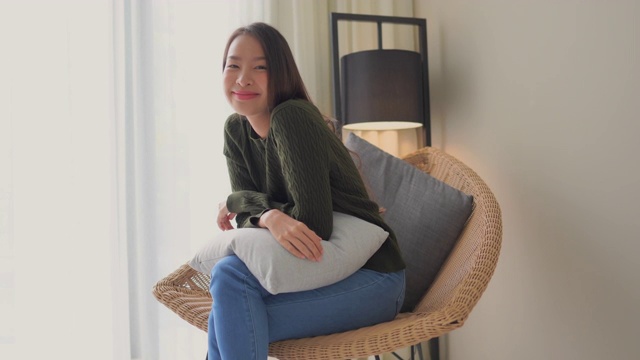 年轻的亚洲女人开心的微笑坐在沙发上视频素材