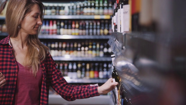 微笑的年轻女子在超市内部的酒精区选择葡萄酒视频素材