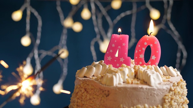 生日蛋糕与40号粉色蜡烛和火花在蓝色背景。慢动作和近景视频下载