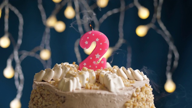 生日蛋糕与2号粉红蜡烛在蓝色的背景。蜡烛吹灭。慢动作和近景视频素材