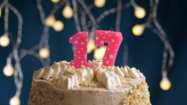 生日蛋糕与17号粉红蜡烛在蓝色的背景。蜡烛吹灭。慢动作和近景视频下载