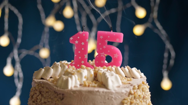 生日蛋糕与15号粉红蜡烛在蓝色的背景。蜡烛吹灭。慢动作和近景视频下载