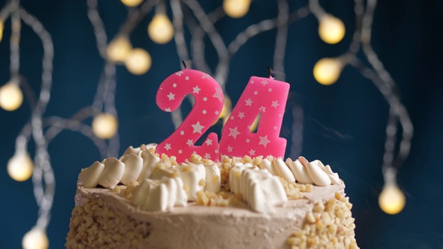 生日蛋糕与24号粉红蜡烛在蓝色的背景。蜡烛吹灭。慢动作和近景视频下载