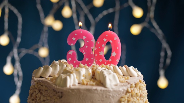 生日蛋糕与30号粉红蜡烛在蓝色的背景。蜡烛吹灭。慢动作和近景视频下载