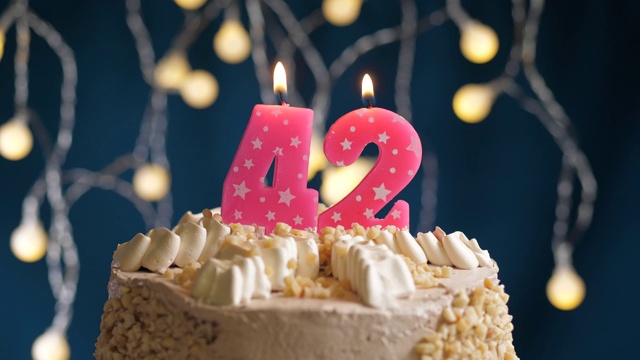 生日蛋糕与42号粉红蜡烛在蓝色的背景。蜡烛吹灭。慢动作和近景视频下载