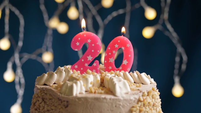 生日蛋糕与20号粉红蜡烛在蓝色的背景。蜡烛吹灭。慢动作和近景视频下载
