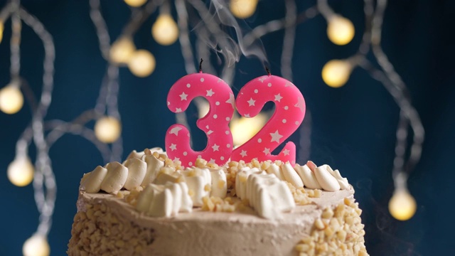 生日蛋糕与32号粉红蜡烛在蓝色的背景。蜡烛吹灭。慢动作和近景视频下载