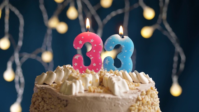 生日蛋糕与33号粉红蜡烛在蓝色的背景。蜡烛吹灭。慢动作和近景视频下载