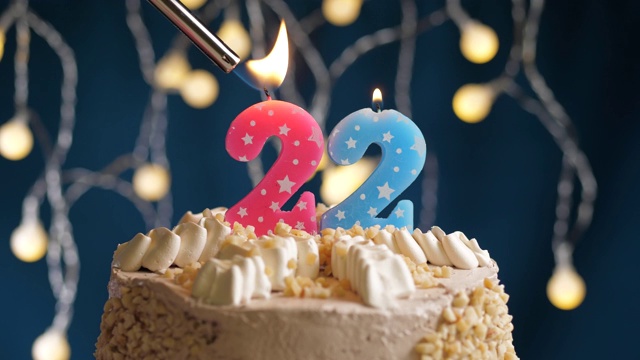 生日蛋糕与22号粉红蜡烛在蓝色的背景。蜡烛被点燃了。慢动作和近景视频素材