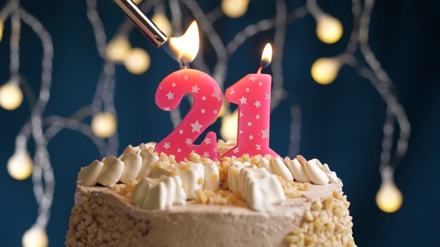 生日蛋糕与21号粉红蜡烛在蓝色的背景。蜡烛被点燃了。慢动作和近景视频素材