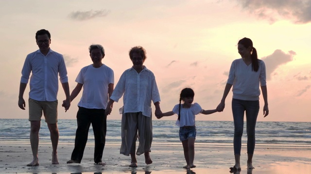新冠肺炎疫情封锁期间，欢乐的亚洲大家庭在沙滩上散步，欣赏日落的海浪。社会距离、家庭、生活方式、社会距离。视频下载