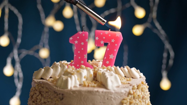 生日蛋糕与17号粉红蜡烛在蓝色的背景。蜡烛被点燃了。慢动作和近景视频下载