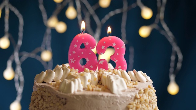 蓝色背景上的63号粉红蜡烛生日蛋糕。蜡烛吹灭。慢动作和近景视频素材