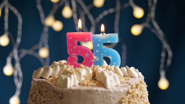 生日蛋糕与55号粉红蜡烛在蓝色的背景。蜡烛吹灭。慢动作和近景视频下载