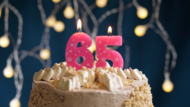 生日蛋糕与65号粉红蜡烛在蓝色的背景。蜡烛吹灭。慢动作和近景视频素材