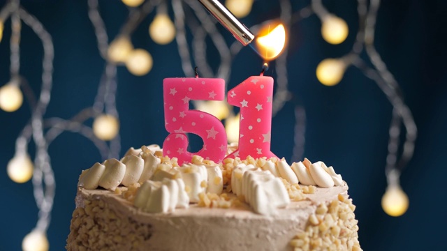 生日蛋糕与51号粉红蜡烛在蓝色的背景。蜡烛被点燃了。慢动作和近景视频下载