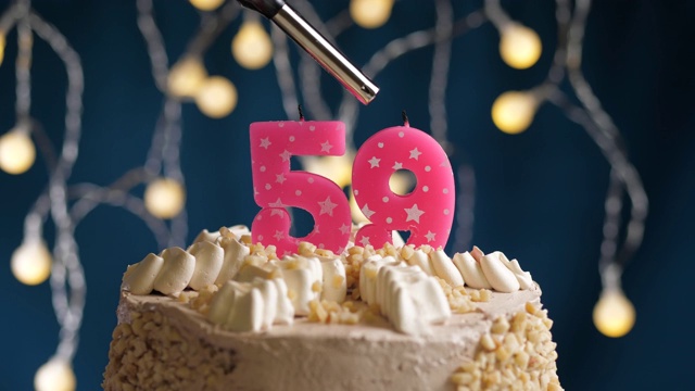生日蛋糕与59号粉红蜡烛在蓝色背景。蜡烛被点燃了。慢动作和近景视频素材