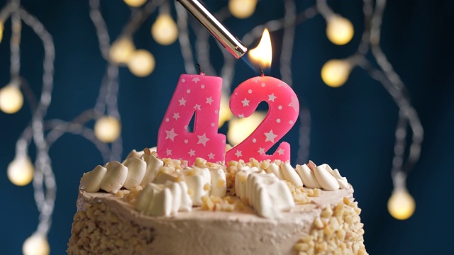 生日蛋糕与42号粉红蜡烛在蓝色的背景。蜡烛被点燃了。慢动作和近景视频下载