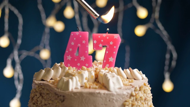 蓝底47号粉红蜡烛生日蛋糕。蜡烛被点燃了。慢动作和近景视频素材