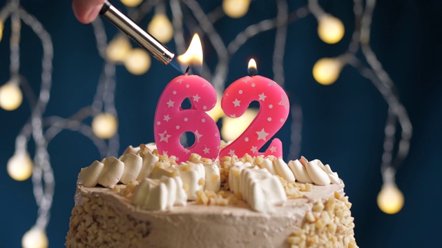 蓝色背景上的62号粉红蜡烛生日蛋糕。蜡烛被点燃了。慢动作和近景视频素材