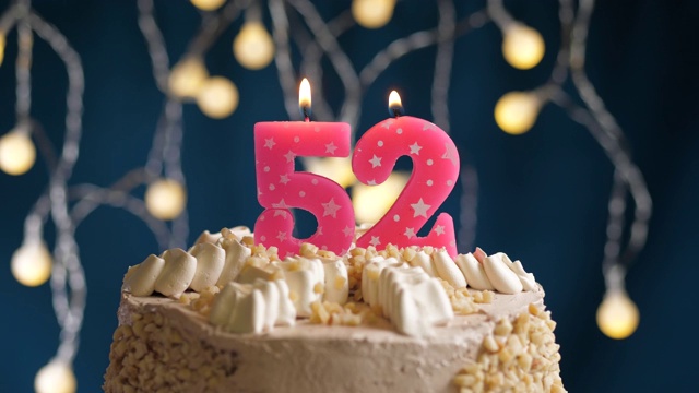 生日蛋糕与52号粉红蜡烛在蓝色的背景。蜡烛被点燃了。慢动作和近景视频下载