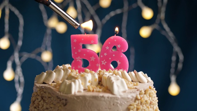 生日蛋糕与56号粉红蜡烛在蓝色的背景。蜡烛被点燃了。慢动作和近景视频素材