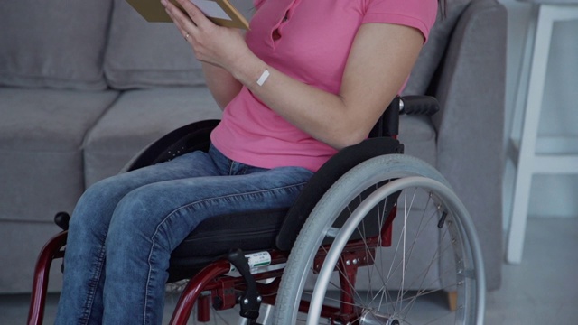 成年妇女坐在轮椅上在家看书视频素材