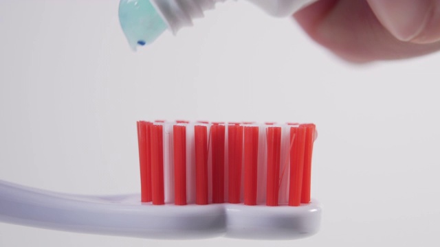 一个男人从白色的牙刷管里挤出一根蓝色的牙膏到塑料牙刷的红色刷毛上视频下载
