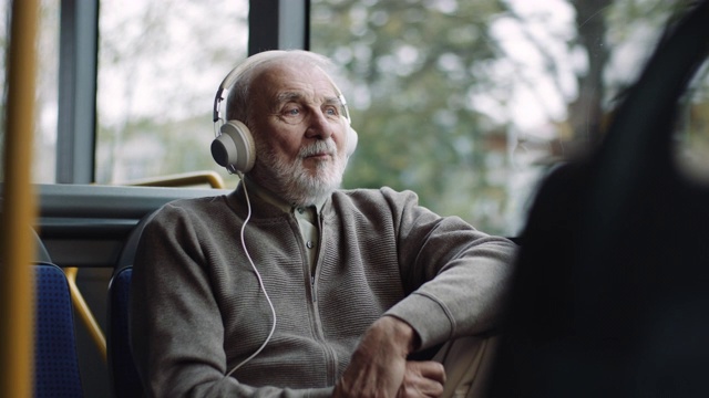 一位老人在公交车上戴着耳机听音乐视频下载