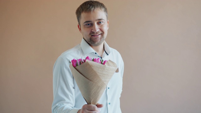 一个浪漫的男人拿着花伸出手微笑着看着镜头的慢镜头视频素材