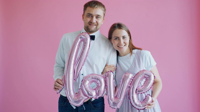 相爱的夫妇抱着字爱在粉红色的背景上感觉幸福相连视频下载