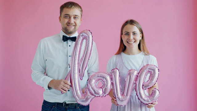一对夫妇的慢动作肖像女孩和男孩持有字爱在粉红色的背景视频下载