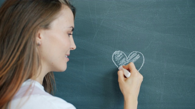 特写的漂亮的年轻女子在黑板上画心形微笑视频下载