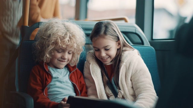一个微笑的男孩和一个女孩在公交车上一起用平板电脑视频素材