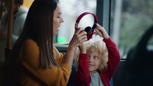 儿子把耳机给妈妈，让她在公交车上听音乐视频素材