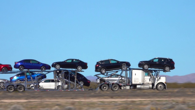 特写:货运卡车载着汽车沿着公路穿越犹他州沙漠。视频下载
