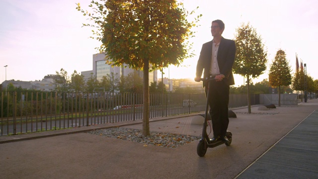 拷贝空间:在一个阳光明媚的早晨，微笑的商人骑着电动滑板车去上班。视频素材