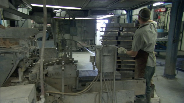 一名生产工人戴着呼吸器和手套把金属板放到传送带上。视频素材