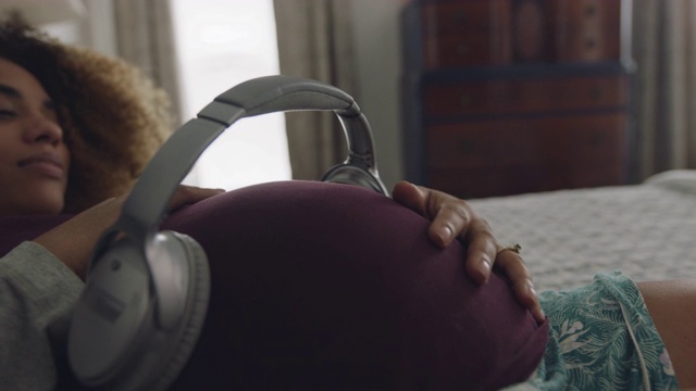 一位孕妇用耳机在怀孕的肚子上摩擦自己的肚子视频素材