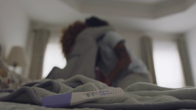 一个怀孕测试阳性的CU躺在床上，背景是一对夫妇拥抱视频素材